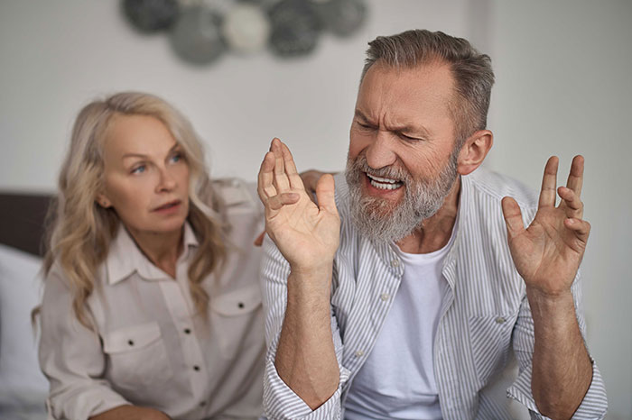 Middle-aged man expressing frustration while woman looks on, illustrating confrontation and breakup themes.