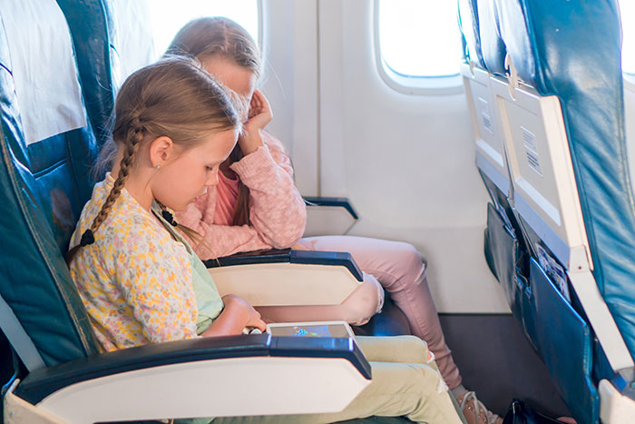 Two children sitting quietly in airplane seats near a window, reflecting a moment about not switching seats on a plane.