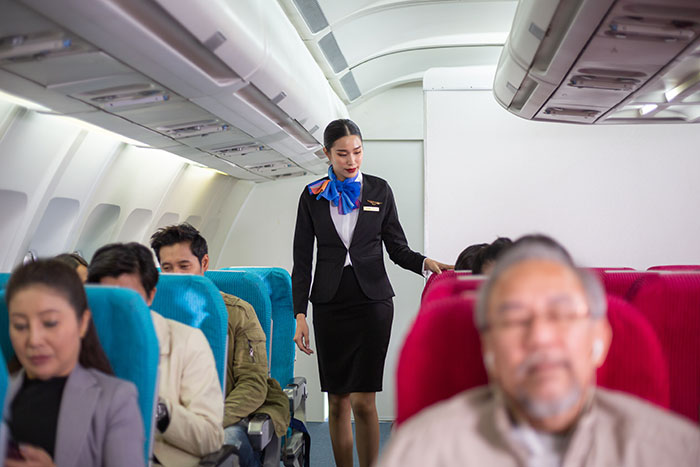 Flight attendant walking down airplane aisle between seated passengers, highlighting airplane seat switch and children issues.