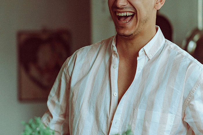 Man wearing striped shirt laughing while pulling a harmless prank in a casual indoor setting.