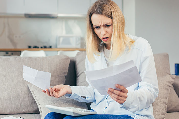 Young woman looking shocked while holding papers and using a calculator, illustrating a prank causing panic and revenge.
