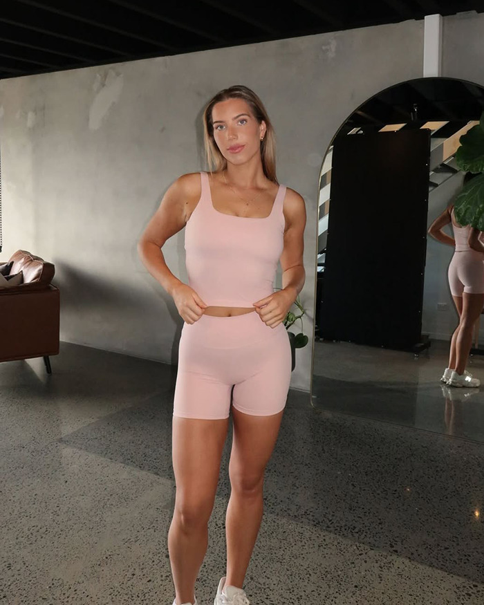 Woman in pink athletic wear standing confidently indoors, showcasing fitness and weight loss transformation journey.