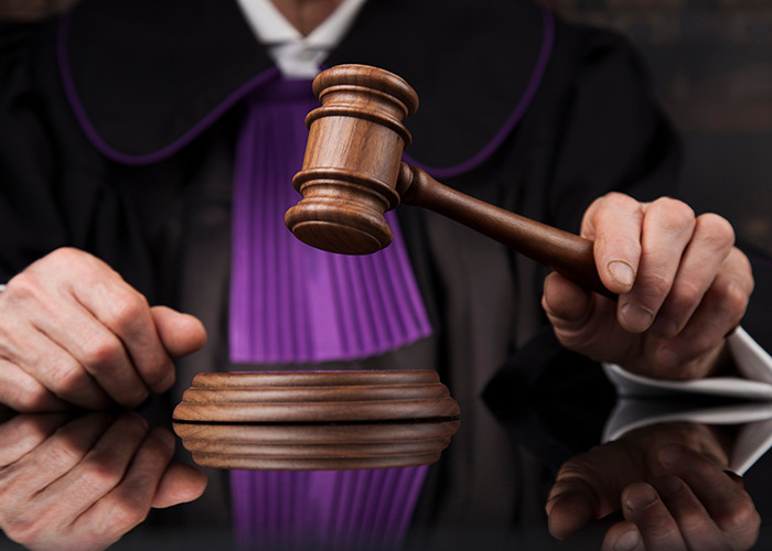 Judge in black robe holding a wooden gavel over sounding block during a sentencing in a courtroom.