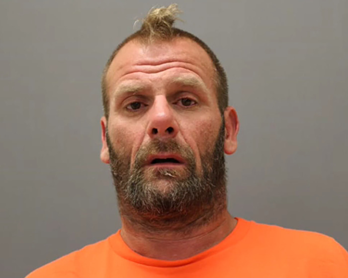 Mugshot of a man with a beard and orange shirt, related to alleged attacker in caring mother jaw injury case.