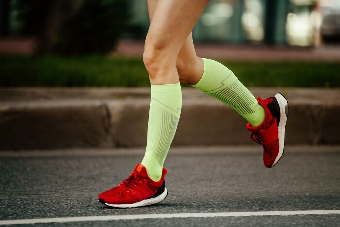 Person running on pavement wearing bright green compression socks and red running shoes, demonstrating active travel hacks.