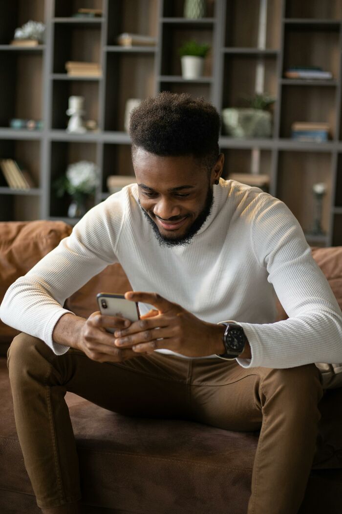 Young man sitting on a couch looking at his phone, reflecting on disrespectful moments with partner’s family.