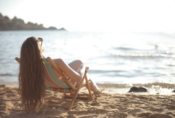Woman with long hair relaxing on a beach chair by the water, reflecting on disrespectful partner family experiences.