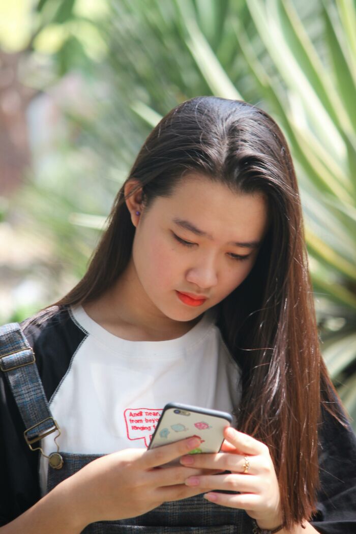 Young woman looking upset while reading a message on her phone about disrespect from partner’s family outdoors.