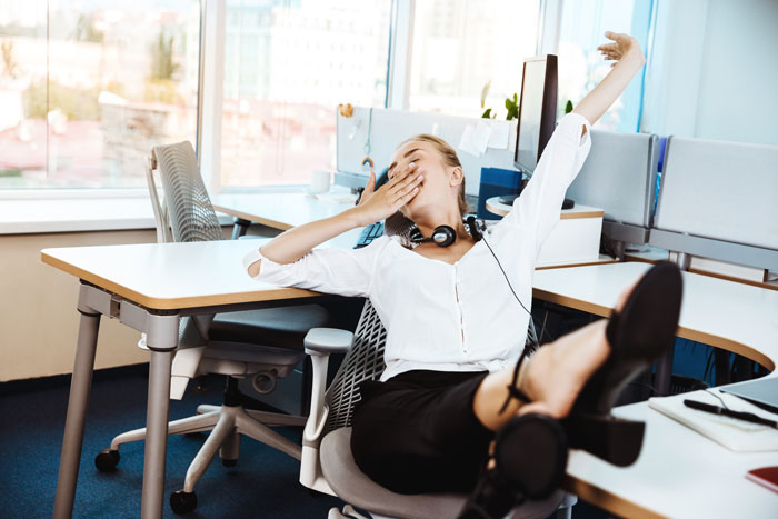 Tired employee yawning and stretching at desk, frustrated with work laptop and unequal treatment in office environment. Tired employee yawning and stretching at desk, frustrated with work laptop and unequal treatment in office environment.