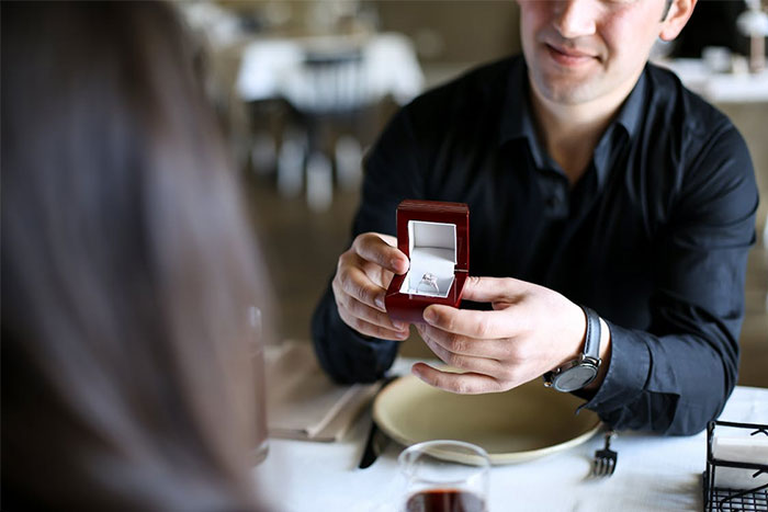 Man in a restaurant holding an open ring box during a date, illustrating servers sharing the worst dates witnessed at work