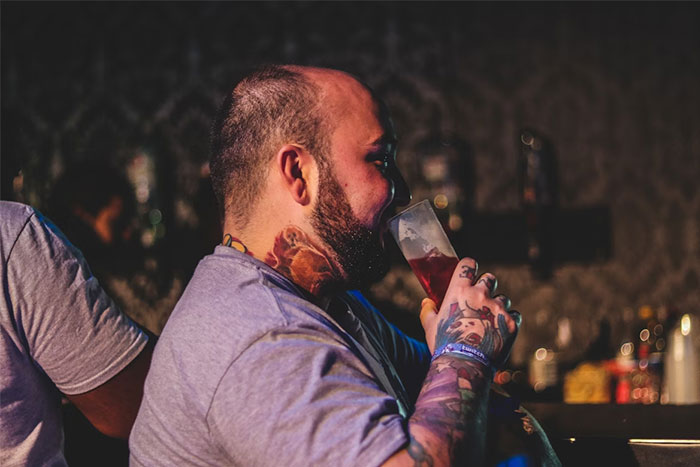 Tattooed server drinking beer behind the bar, illustrating servers sharing the worst dates they witnessed at work.