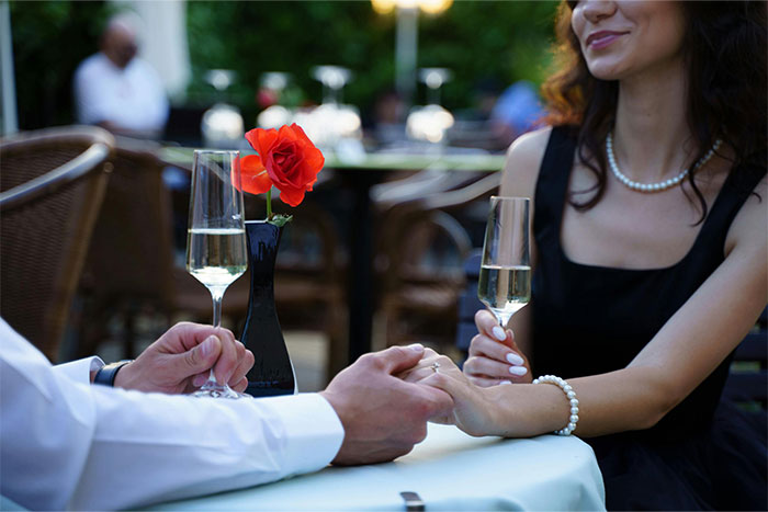 Couple holding hands at a romantic restaurant table with champagne, illustrating servers witnessing worst dates at work.