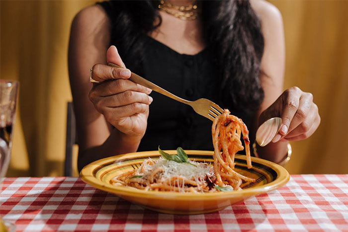 Woman enjoying a plate of spaghetti at a restaurant, illustrating servers sharing the worst dates they witnessed at work.