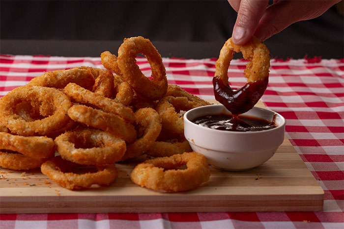 Close-up of a hand dipping an onion ring into sauce on a wooden board, illustrating servers sharing worst dates at work.