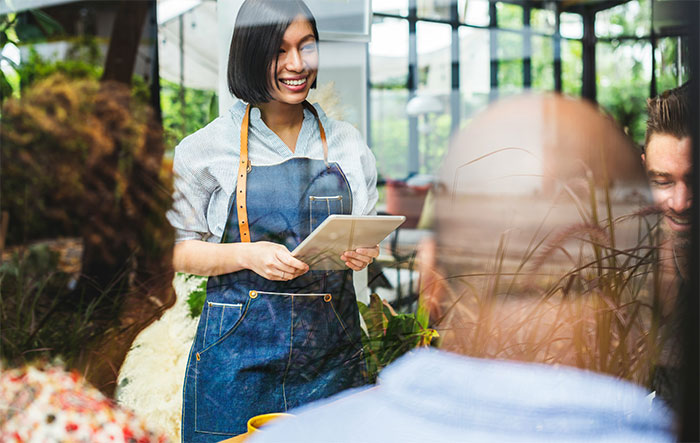 Server smiling and holding a tablet while interacting with customers, sharing worst dates witnessed at work.