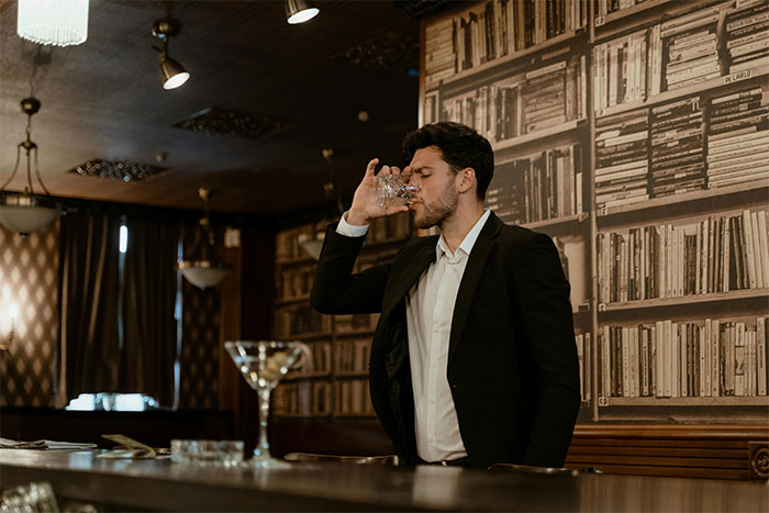 Man in black suit drinking at bar, representing servers sharing the worst dates they witnessed at work.
