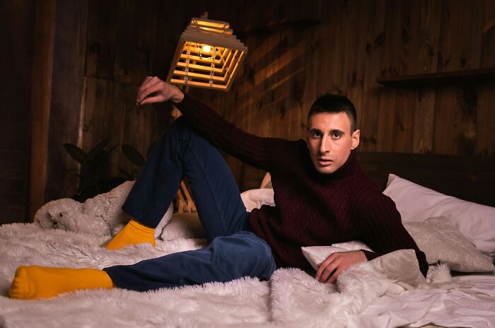 Young man with intense expression lying on a bed in cozy room, illustrating awkward moments of nice guys turning creepy.