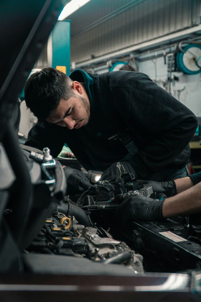 Man focused on car engine repair in a garage, illustrating awkward moments with nice guys turning creepy.