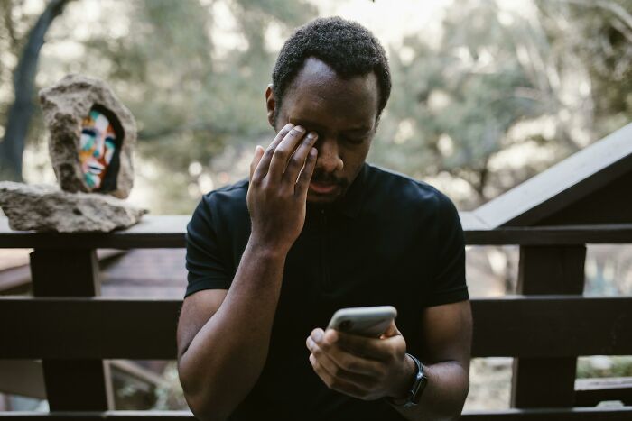 Man in black shirt looking stressed while checking phone outside, illustrating awkward moments of nice guys turning creepy.