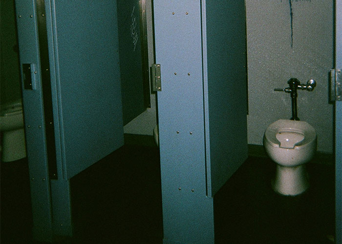 Public restroom stalls with blue partitions and a toilet, illustrating workplace behavior mishaps and office dynamics.