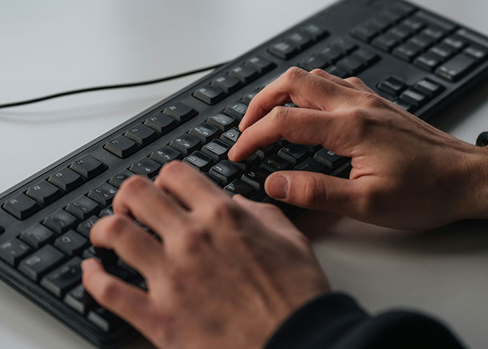 Person typing on a black keyboard, illustrating work behavior for people who don’t know how to behave at work.