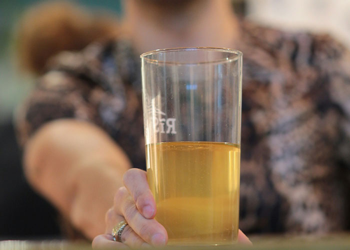 Person holding a pint glass of beer at a table, illustrating behavior in a workplace setting.