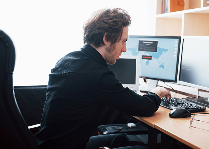 Man working at dual monitors in an office setting, illustrating people who don’t know how to behave at work.