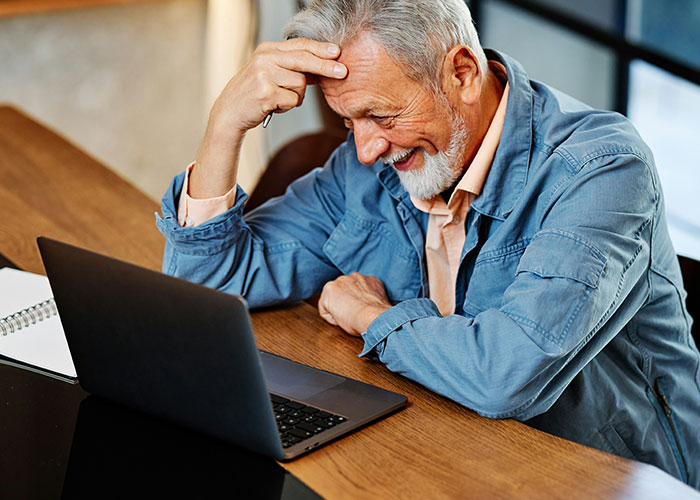 Older man frustrated at laptop displaying poor work behavior in an office setting reflecting how not to behave at work.
