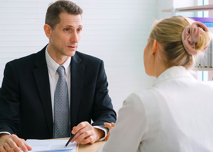 Man in a suit and tie discussing workplace behavior with a woman in a white blouse during a professional meeting.