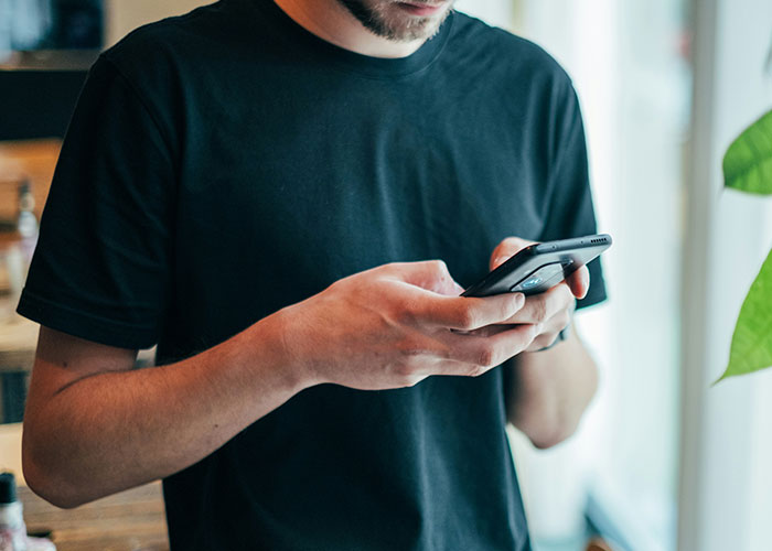Man in a black shirt using a smartphone near a window showing typical work behavior and office culture.