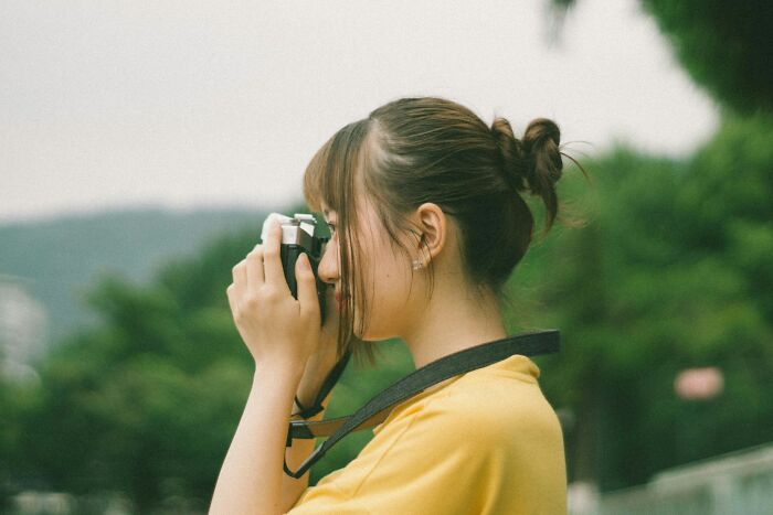 Young woman in a yellow shirt taking photos outdoors, symbolizing creative ways people got back at their cheating exes.