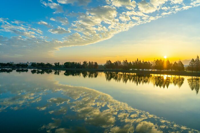 Sunrise over a calm lake with trees reflecting, illustrating the best time to buy a plane ticket for cheapest airfare.