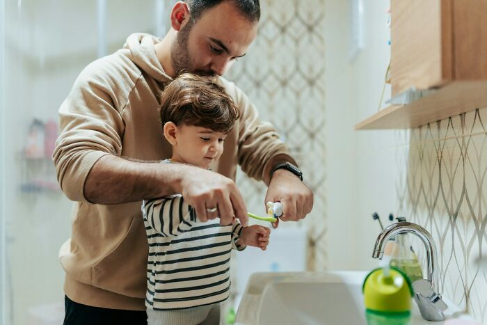 Man helping young boy brush teeth in a bathroom illustrating moments police got dragged into utter nonsense.