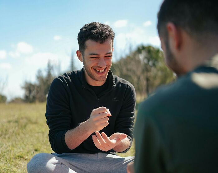 Two men laughing and playing a hand game outdoors, illustrating weird things couples started doing together.