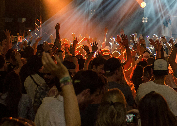Crowded concert scene with people raising hands and enjoying live music under vibrant stage lighting. - 1