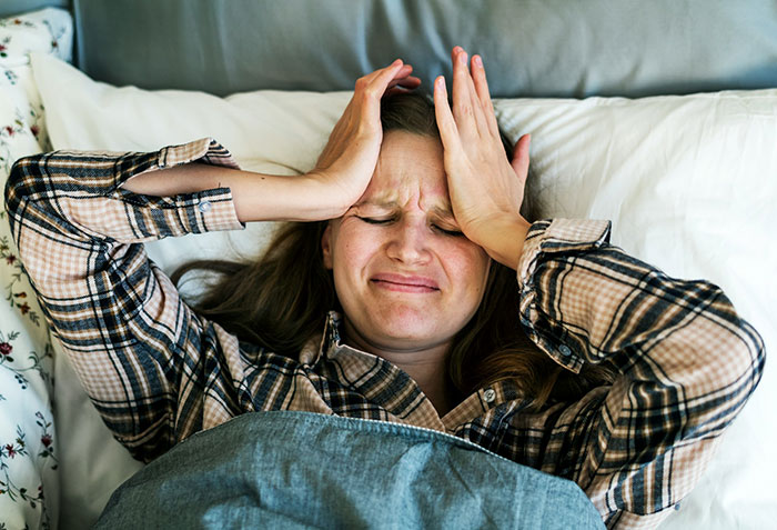 Stressed tired mom lying in bed with hands on forehead, expressing frustration and honest confession feelings.