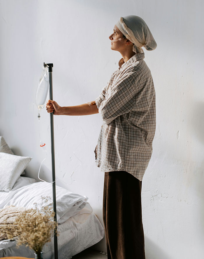 Teen cancer patient wearing headscarf receiving IV treatment in a bedroom, illustrating family upset over head shaving support.