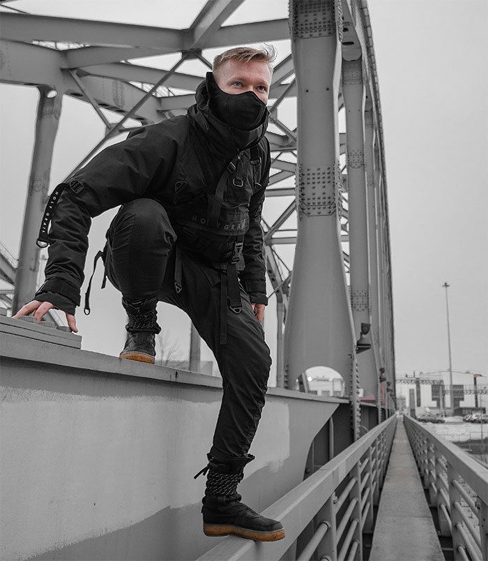 Young man dressed in black streetwear and mask climbing on bridge railing, capturing boomer complains about stranger’s pants concept. - 14