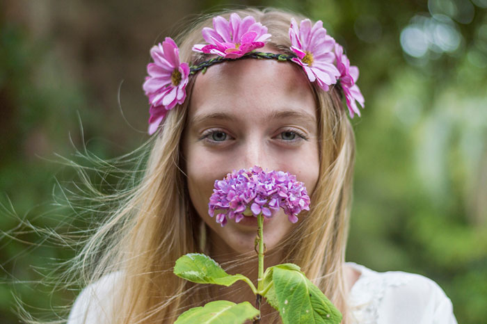 Young woman wearing flower crown, holding purple flower close to her face, looking stunned in outdoor natural setting - 11