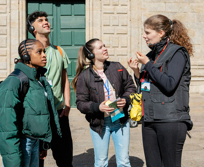 Group of tourists wearing headsets listening to their guide during a city tour, tourists discuss after one overslept three days in a row. - 1