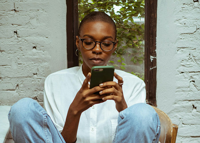 Young woman with glasses sitting casually, focused on her phone, reflecting a story about a half-sister and wedding gift. - 1