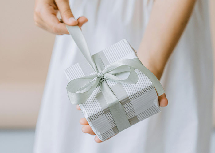 Woman holding a wrapped wedding gift with a silver ribbon, symbolizing expectations despite family wedding drama. - 5