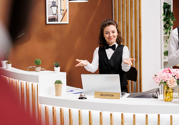 Hotel employee smiling confidently at reception desk, using her power to handle guest's cheating boyfriend situation.