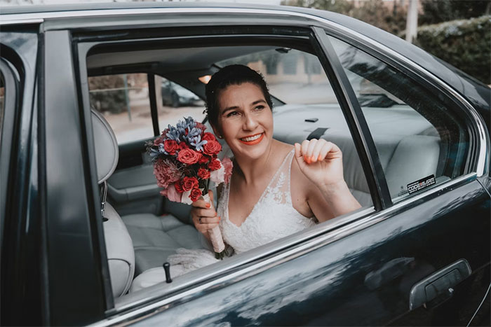 Bride in wedding dress holding bouquet, smiling confidently while sitting in the backseat of a car on her wedding day. - 10