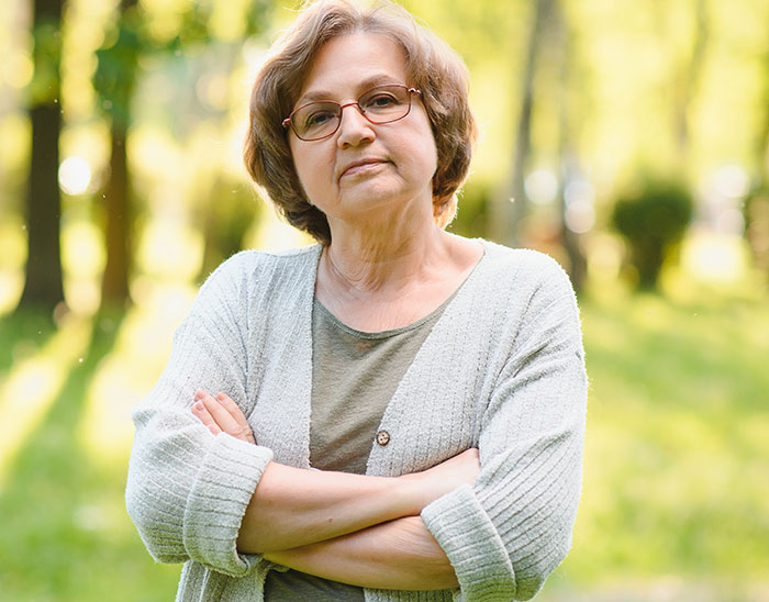Middle-aged woman with glasses and crossed arms standing outdoors, representing a mom involved in gaming store sword sales. - 1