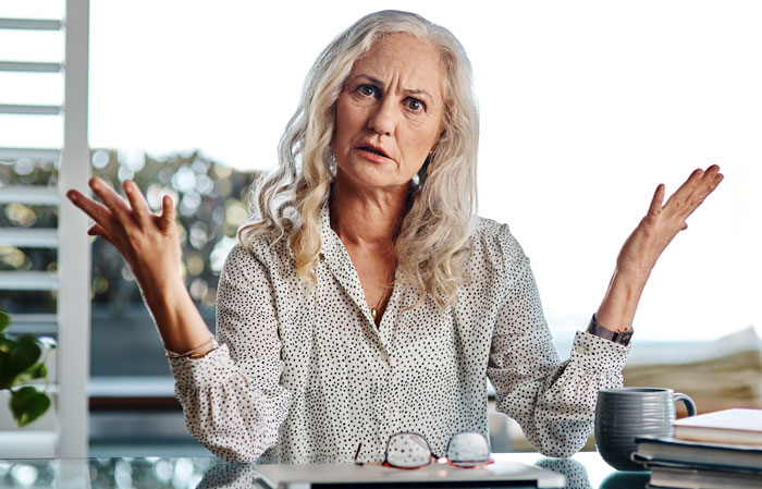 Older woman with gray hair and polka dot blouse raising hands, seeking advice after CPS threats from mother-in-law Older woman with gray hair and polka dot blouse raising hands, seeking advice after CPS threats from mother-in-law