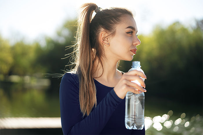 Young woman holding a water bottle outdoors in bright sunlight, highlighting concerns about hydration in high heat conditions. Young woman holding a water bottle outdoors in bright sunlight, highlighting concerns about hydration in high heat conditions.