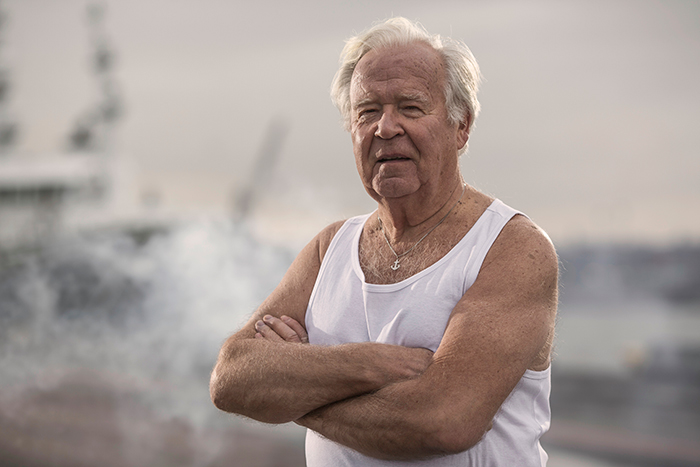 Older man with white hair and tank top standing with arms crossed, related to boomers breaking into barbershop incident. Older man with white hair and tank top standing with arms crossed, related to boomers breaking into barbershop incident.