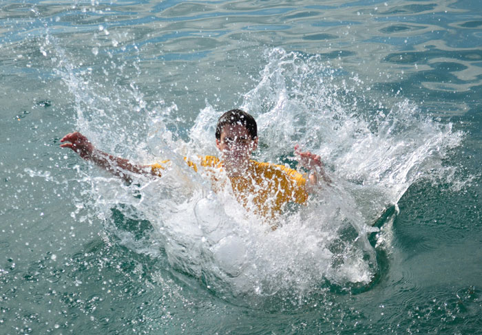Person in yellow shirt splashing water while swimming, illustrating tips to stay safe and alive in water activities.