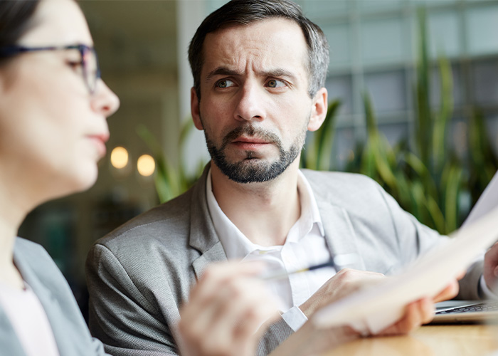Man in gray suit reviewing documents with concerned expression during a discussion about ridiculous employee complaints for managers and HR.